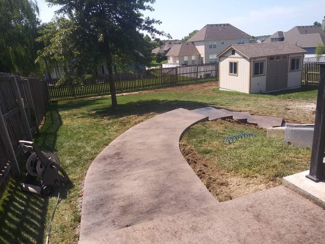 A concrete walkway in a backyard with a house in the background