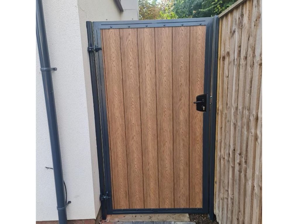 Light oak effect composite side gate set in a grey powder-coated metal frame against a timber fence