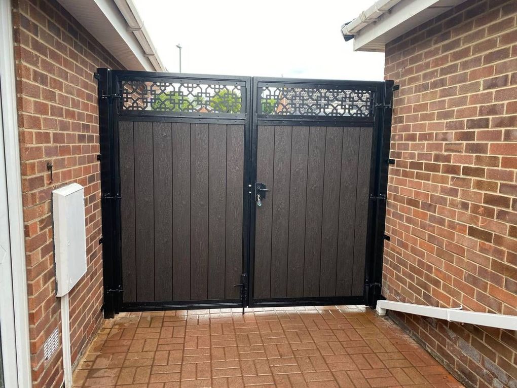 Chocolate composite driveway gates with a decorative screen along the top, fitted between brick walls