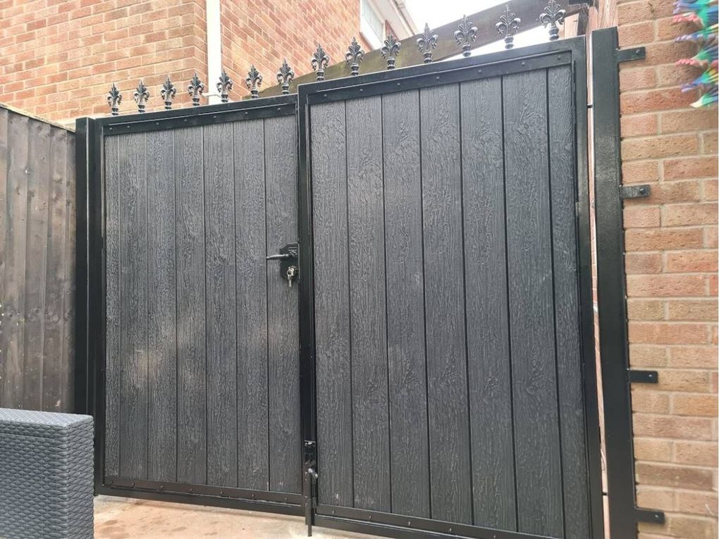 Dark composite driveway gates with fleur-de-lis finials and a drop bolt