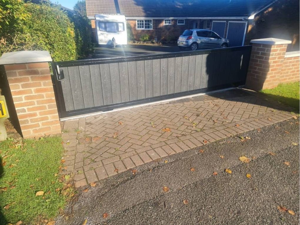 Low sliding composite driveway gate between brick piers with stone caps