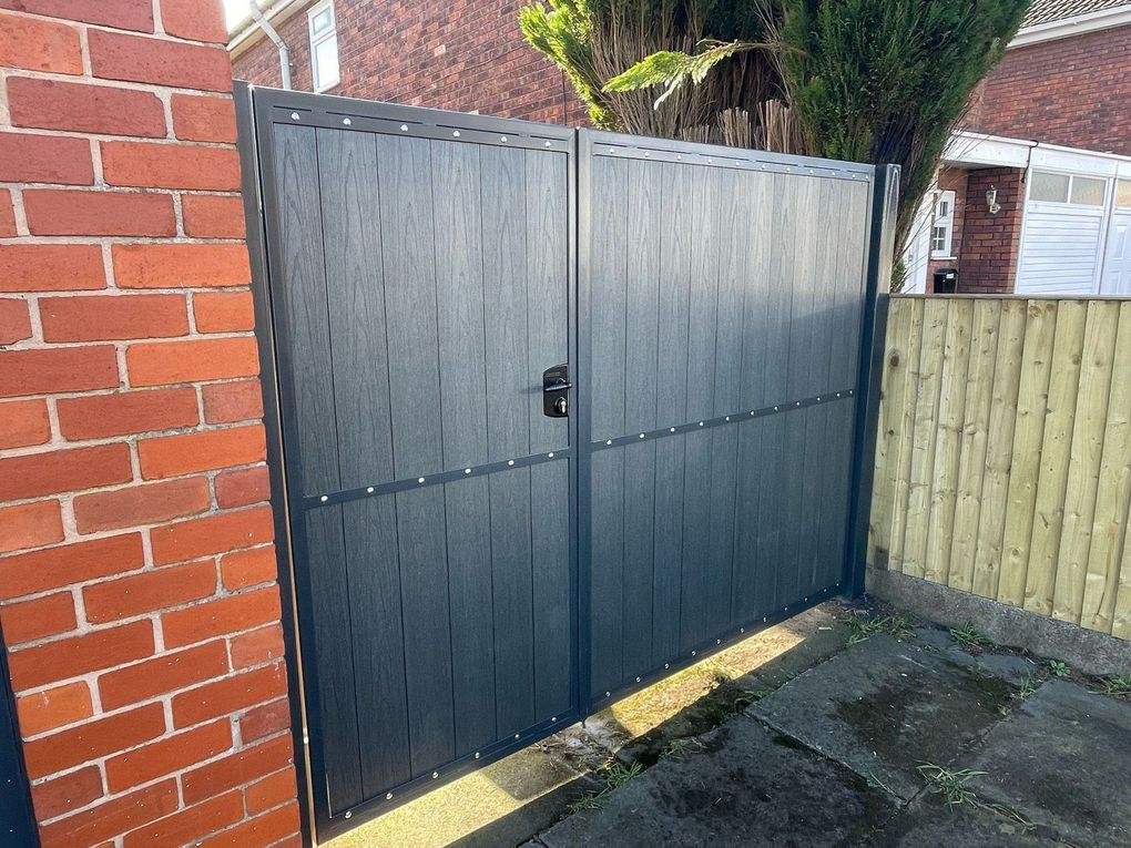 Anthracite grey woodgrain composite driveway gates with a mid rail, hung between a brick pier and a timber fence