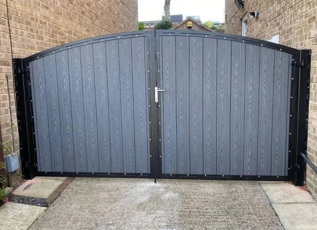 Arched grey composite driveway gates between brick pillars