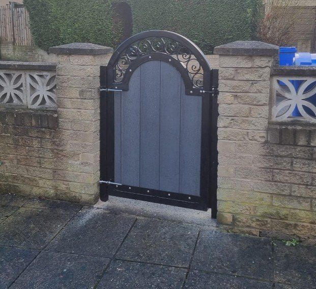 Arched grey composite garden gate with a scroll-work top, hung between stone piers