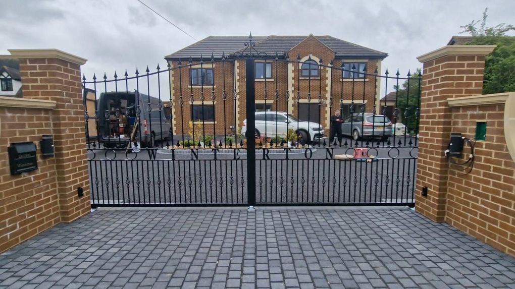 Black metal driveway gates with a curved top between brick piers