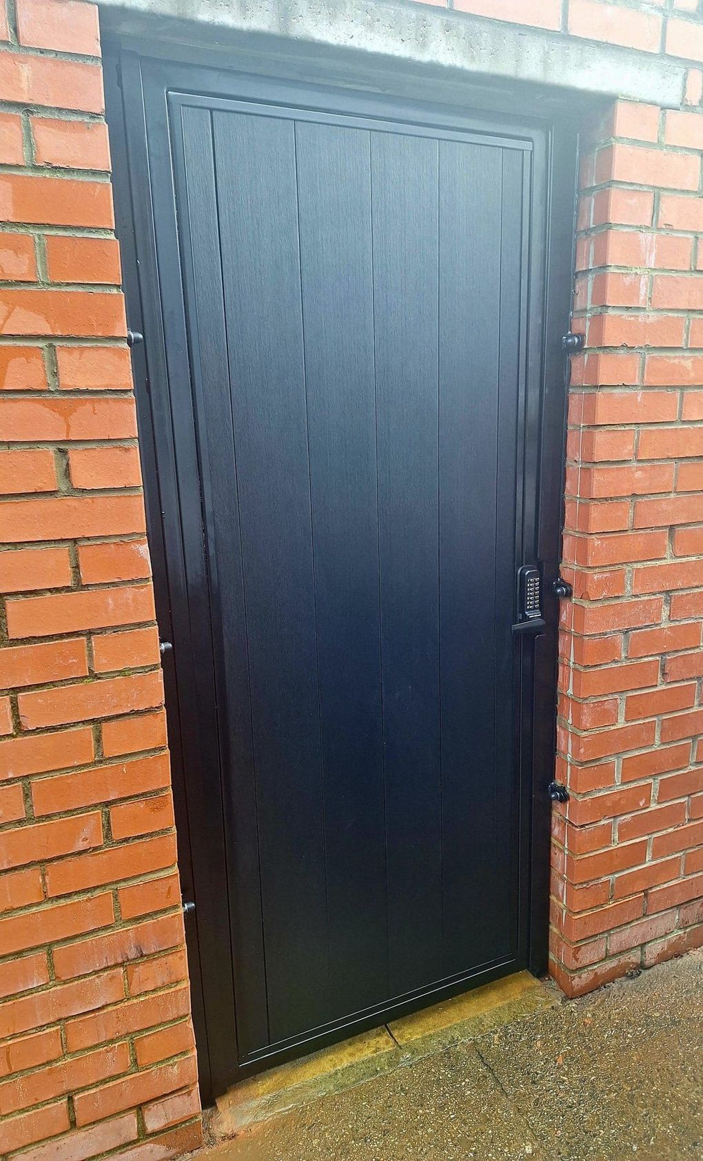 Black composite gate with a keypad lock, set into a brick opening
