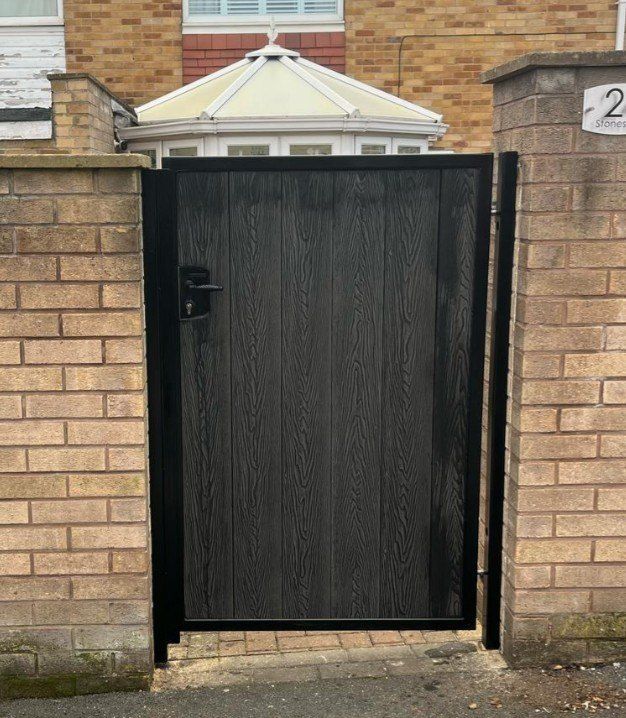 Black woodgrain composite pedestrian gate hung between brick piers