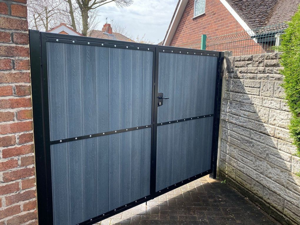 Blue-grey woodgrain composite driveway gates with a mid rail, between a brick pier and a stone-effect wall