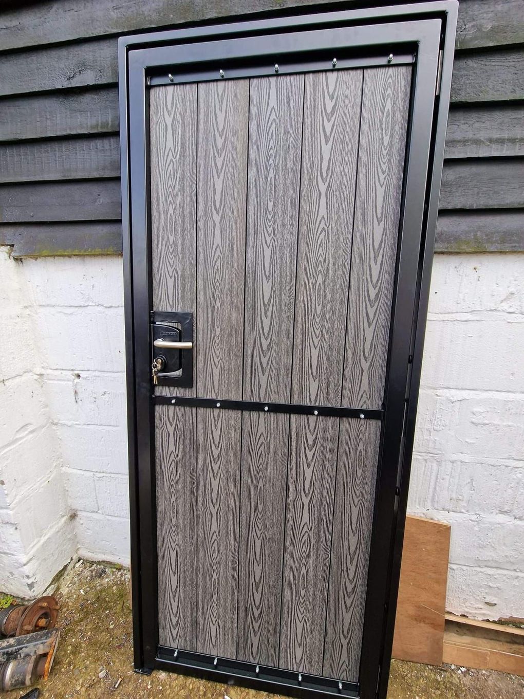Finished composite gate leaf standing against a wall, dark grey boards in a black powder-coated frame