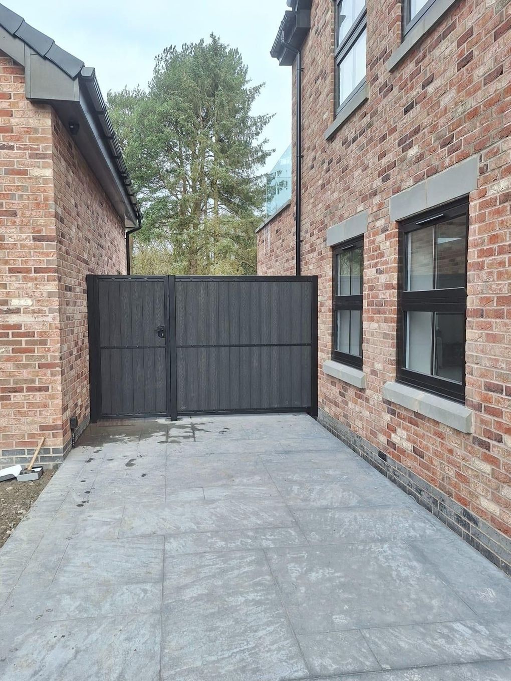Dark composite pedestrian and driveway gates closing off a paved side drive between two brick buildings