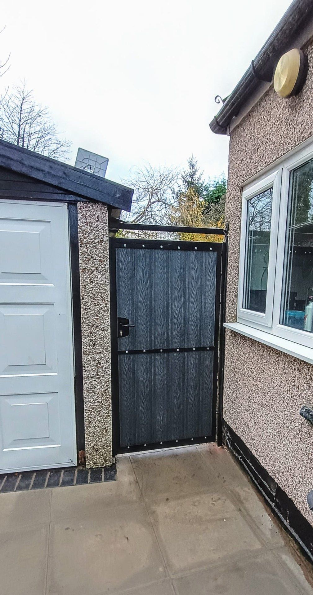 Dark woodgrain composite side gate with a mid rail between a garage and a pebbledash house