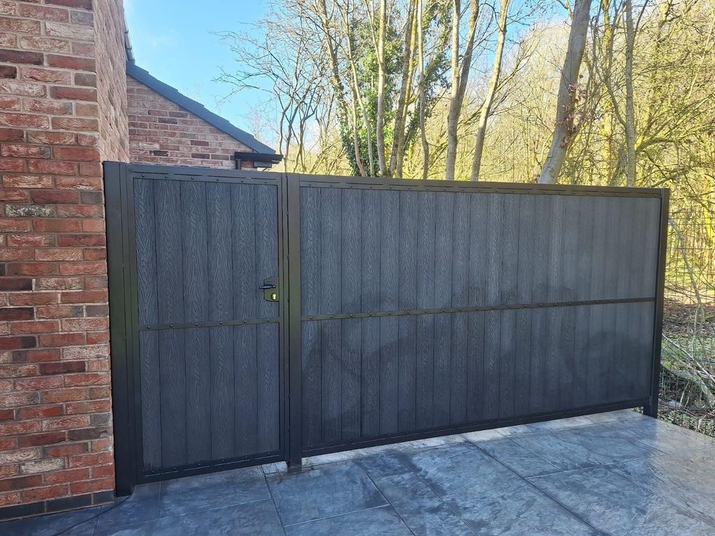 Dark woodgrain composite driveway gate with a matching pedestrian gate beside a new brick house