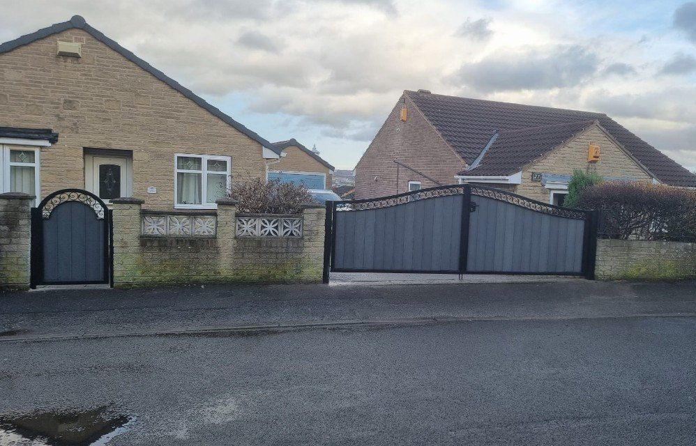 Grey composite driveway gates with a scroll-work top and a matching arched pedestrian gate in a low front wall