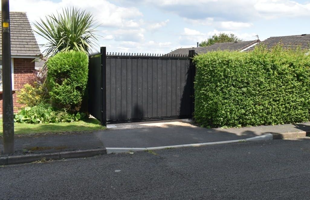 A black gate is sitting on the side of a road next to a hedge.