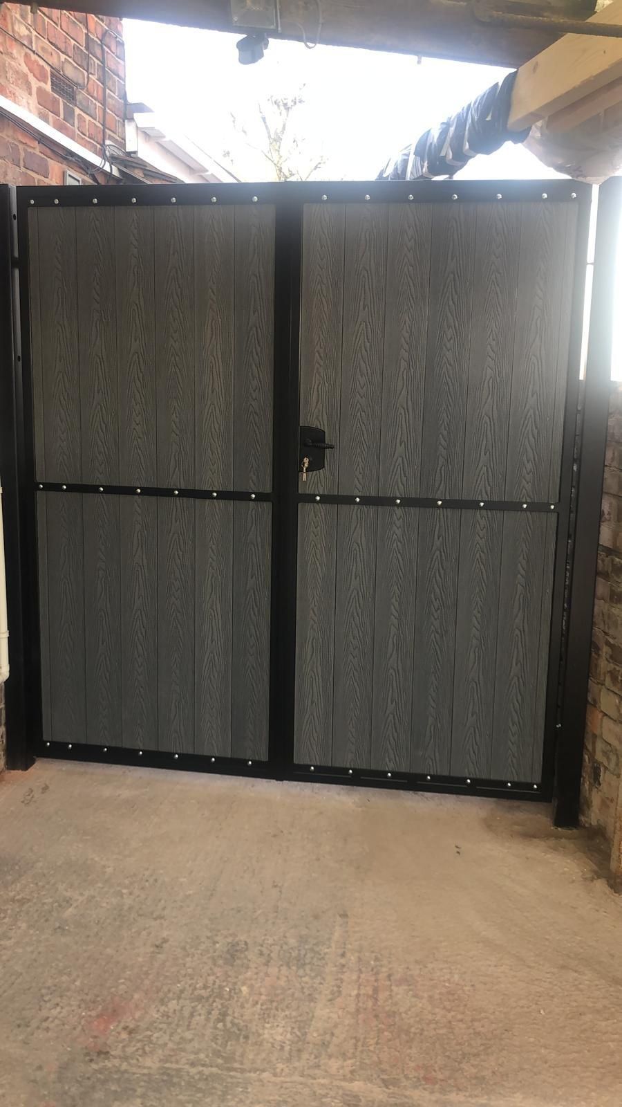 Grey woodgrain composite double gates with a mid rail, fitted under a covered carport