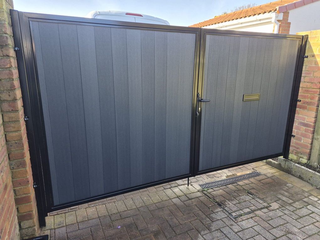 Grey composite driveway gates, one wide leaf and one narrower leaf with a letterbox, on a block-paved drive