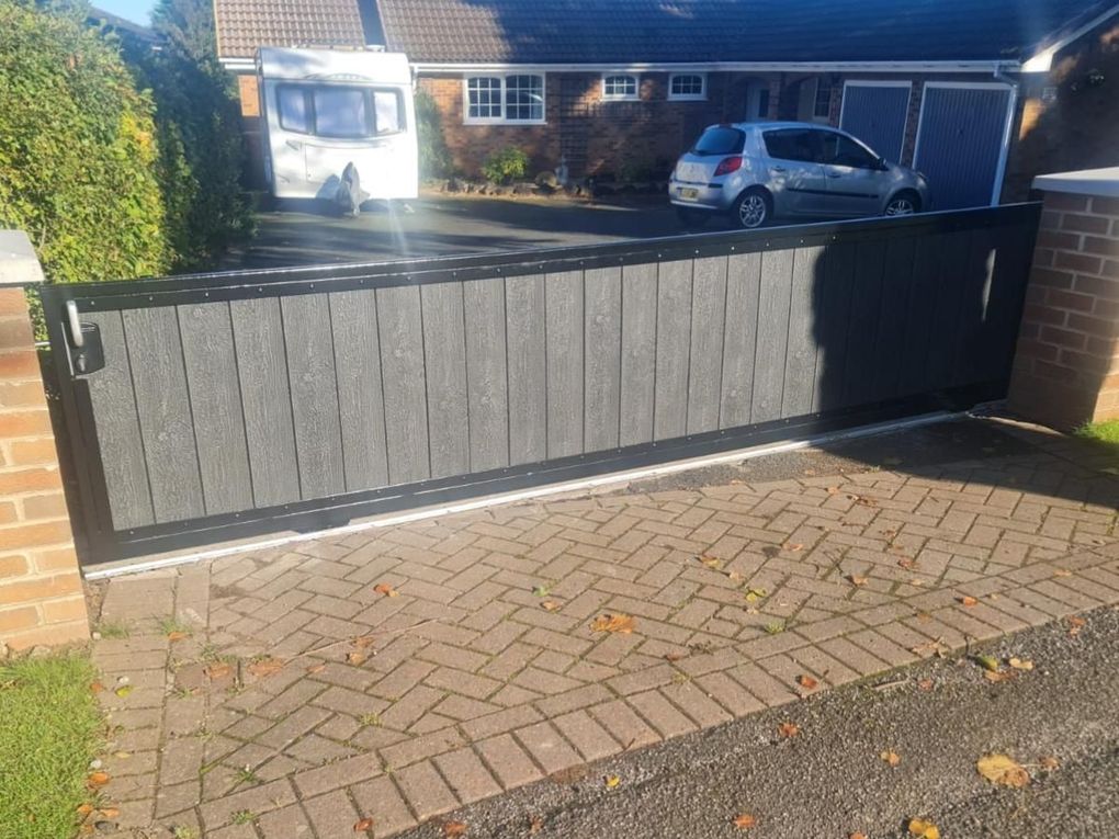 Anthracite grey composite sliding driveway gate closed across a block-paved entrance
