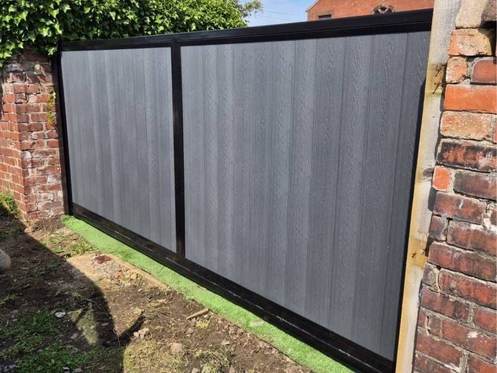 Light grey composite double driveway gates with a black powder-coated frame, hung between brick piers
