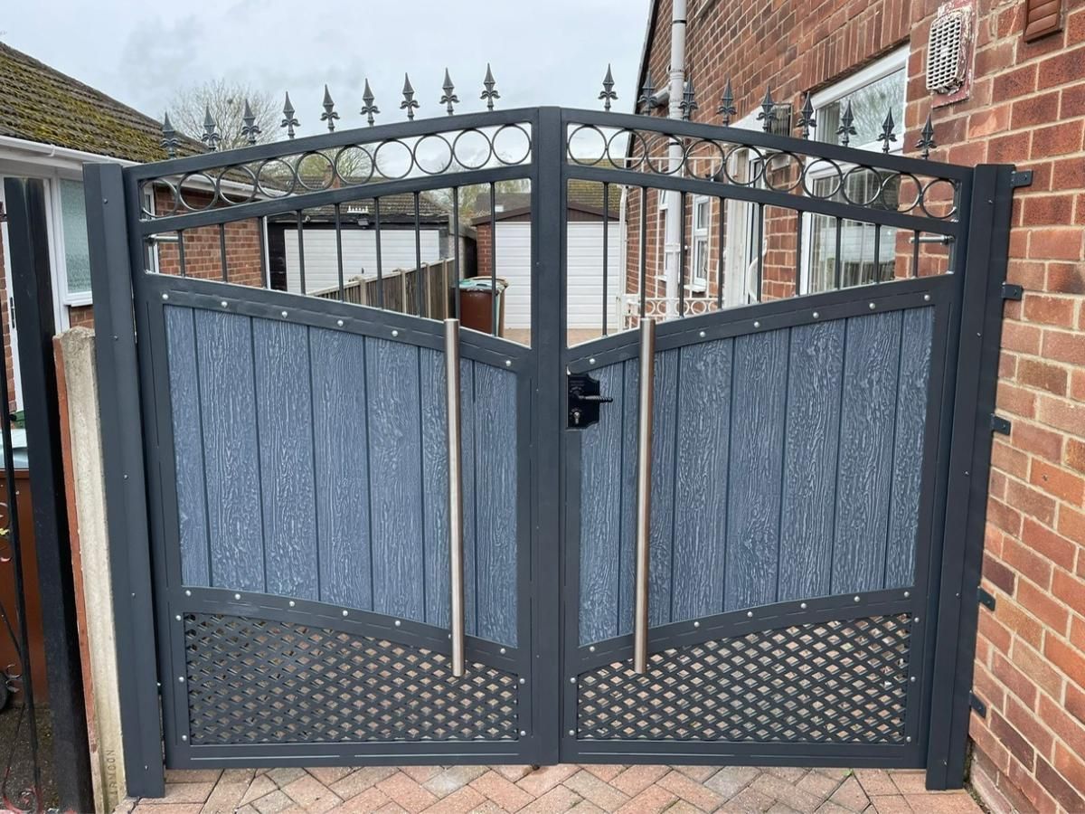Light grey composite driveway gates with an anthracite grey frame, an arched top rail with decorative circle detail and fleur-de-lis finials, lattice infill along the bottom and brushed stainless steel pull handles, in Manchester