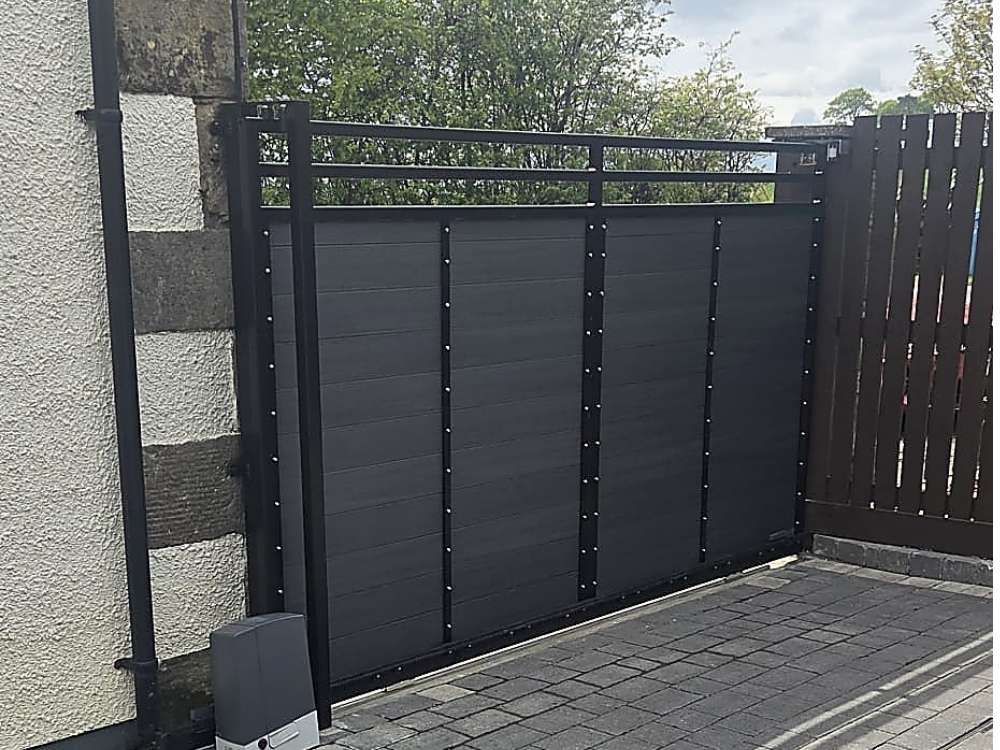 Anthracite grey composite sliding driveway gate running against a stone wall