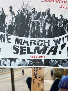 Banner reading “We March with Selma! 1965-2015” at a civil rights march under a raised fist sign