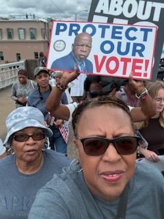 Crowd holds “Protect Our Vote!” sign at a public rally.