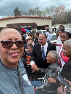 Woman in sunglasses smiling for a selfie with a crowd outdoors near a building