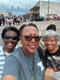 Three people smiling for a selfie on a busy street outdoors