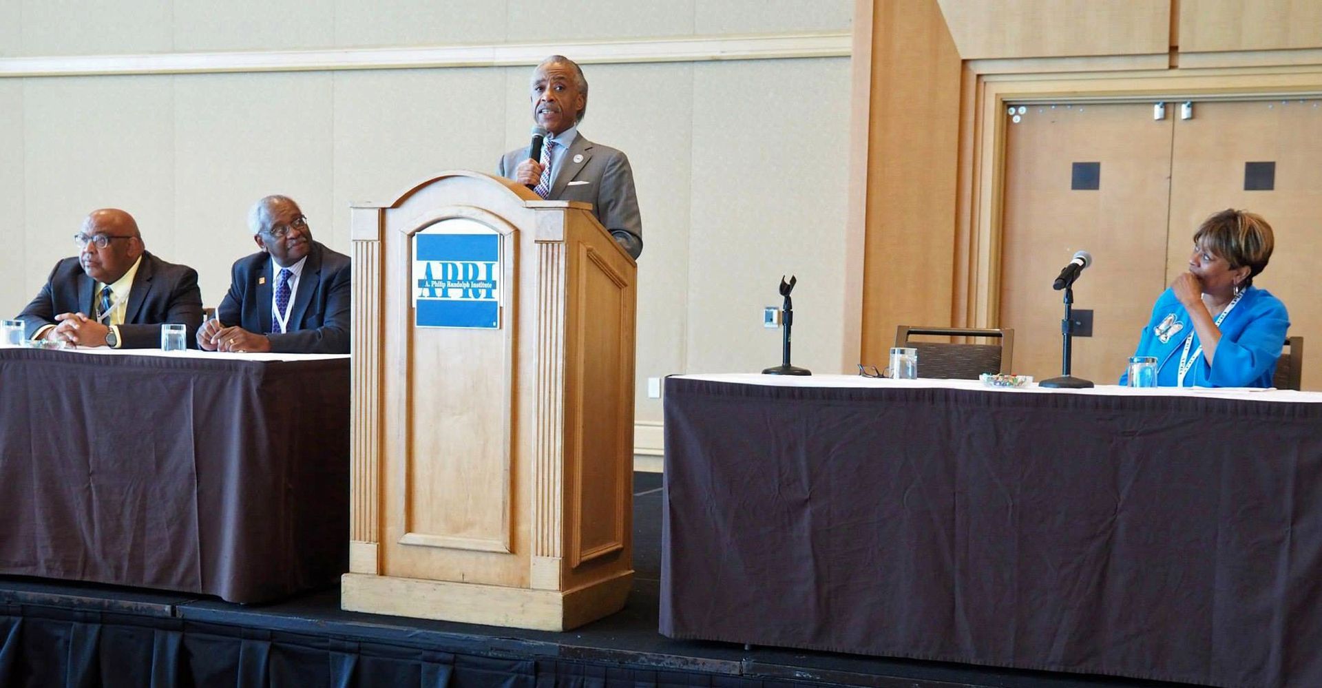 Reverend Al Sharpton giving a speech at a podium with a blue sign on it