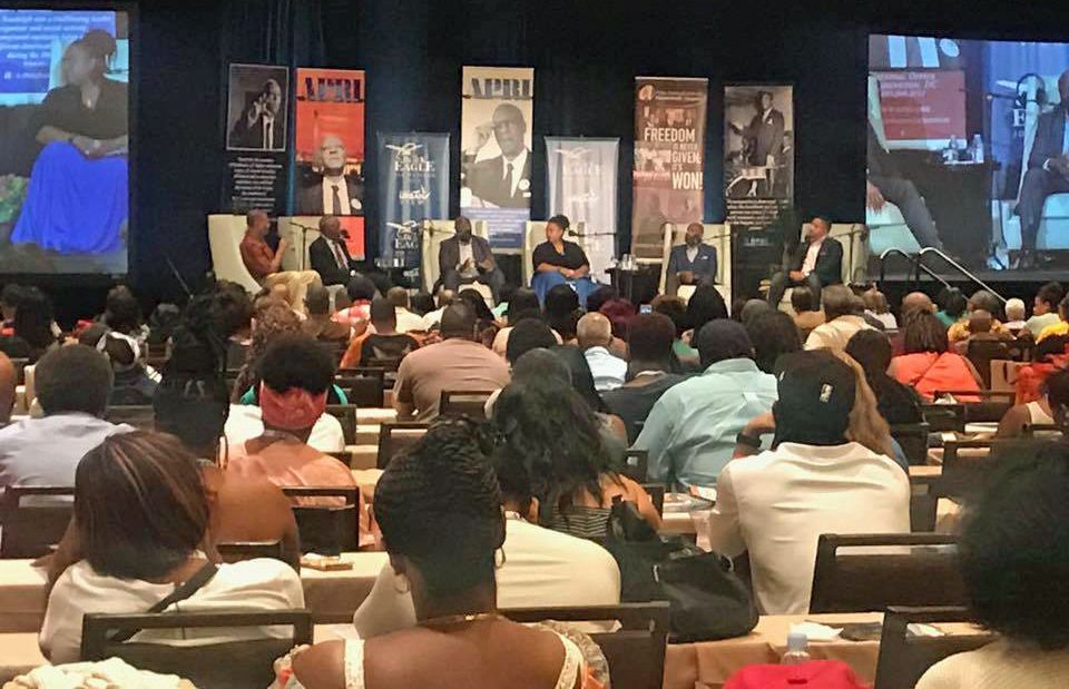 A large group of people are sitting in a conference room watching a presentation.