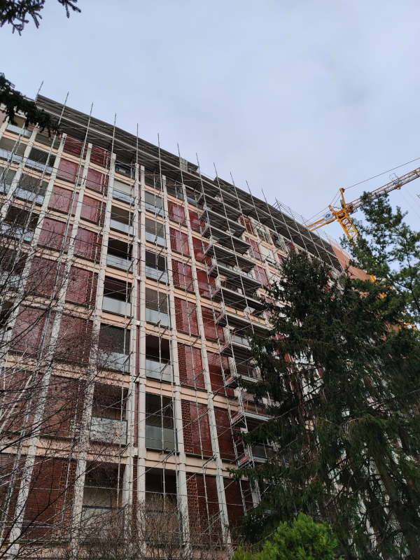 Grattacielo in costruzione con impalcature e gru sullo sfondo di un cielo nuvoloso.