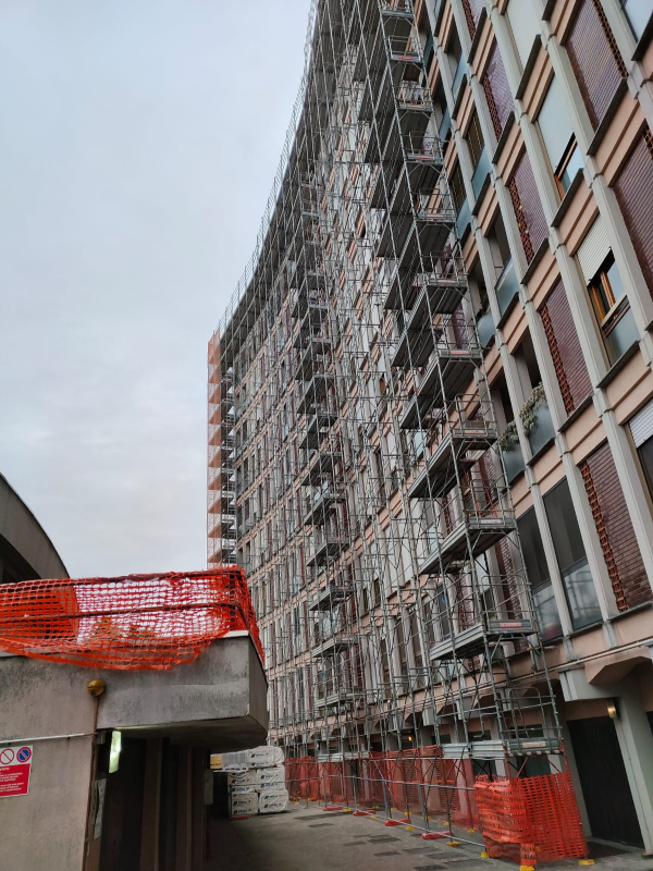 Edificio residenziale curvo in costruzione, con reti di sicurezza arancioni e impalcature lungo la strada.