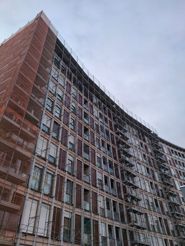 Alto e moderno palazzo residenziale con mattoni rossi e finestre in vetro, visto dal basso contro un cielo nuvoloso.