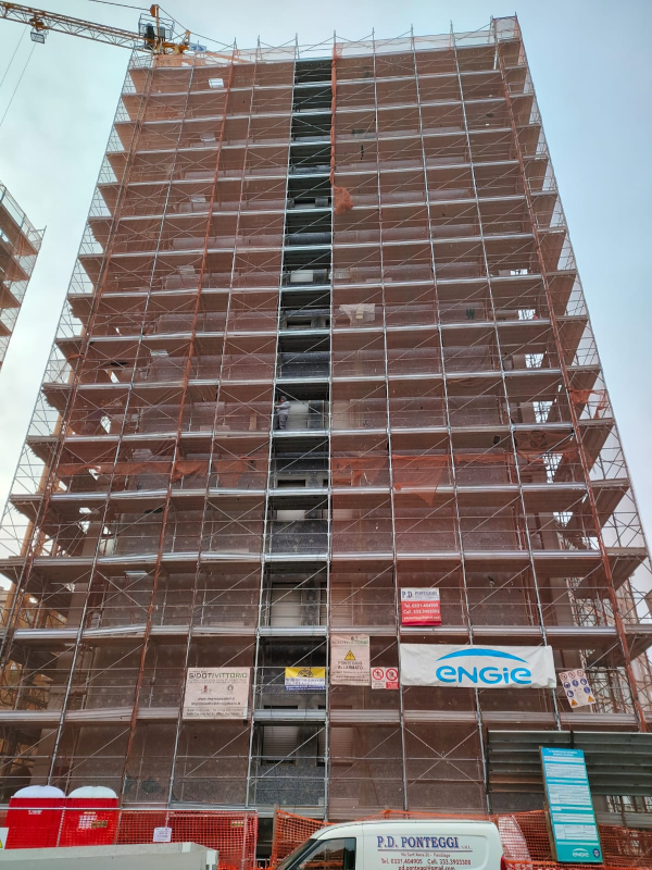 Un grattacielo avvolto da impalcature e reti di sicurezza durante la costruzione, con una gru in alto.