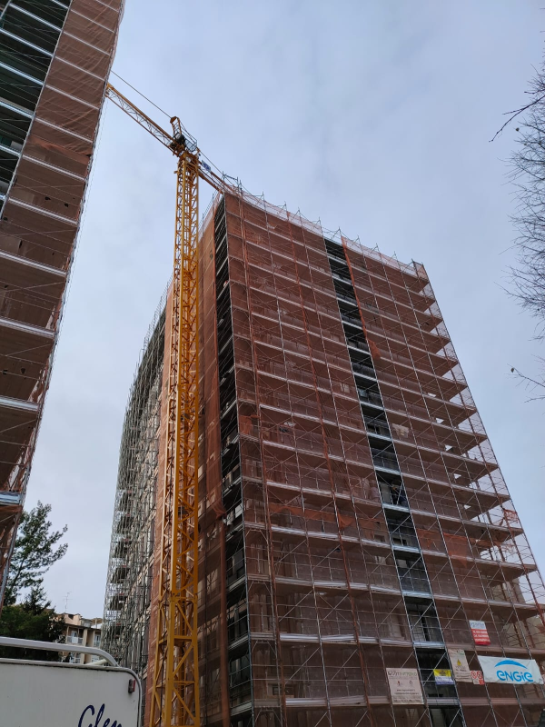 Grattacielo in costruzione con impalcature e gru sullo sfondo di un cielo nuvoloso.