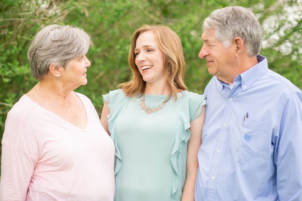 Three people smiling together outdoors, with greenery in the background.