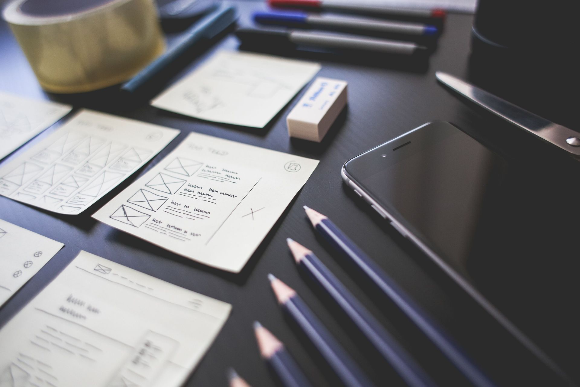 Desk with sketch papers, pencils, and a smartphone arranged on a dark tabletop