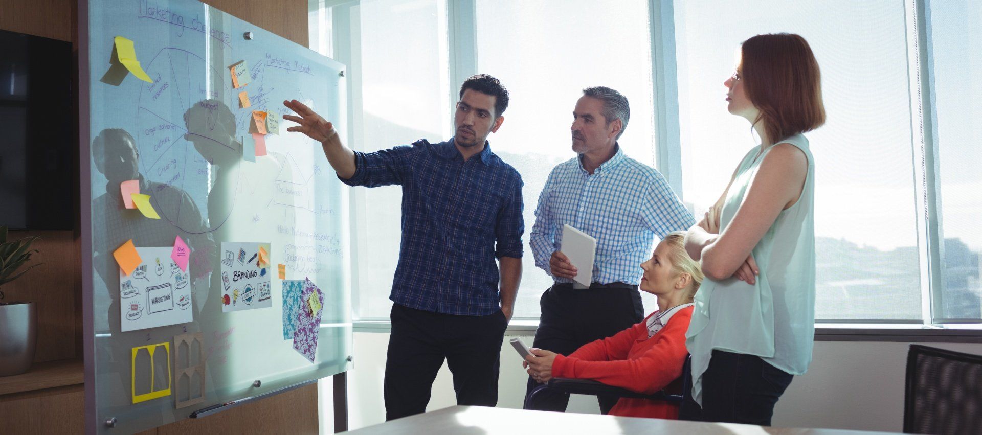 A group of people are standing around a table looking at a whiteboard.