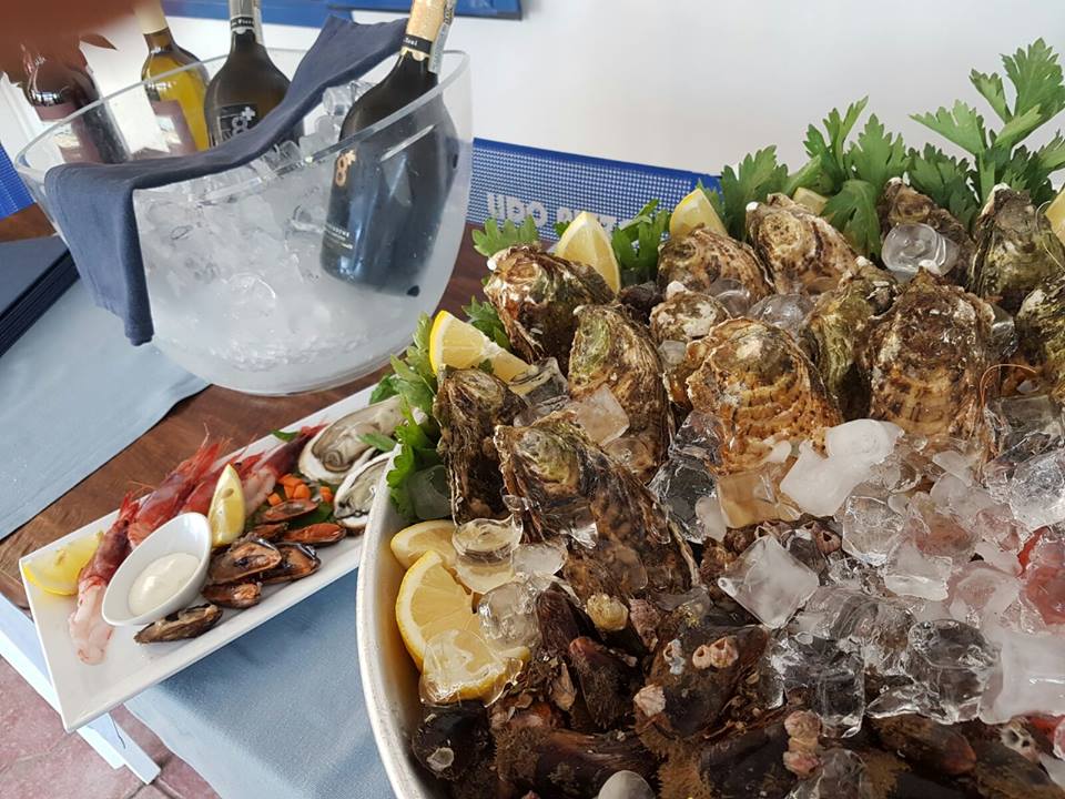 Piatto di frutti di mare su ghiaccio tritato con ostriche, spicchi di limone e un refrigeratore per bottiglie con bottiglie di vino.