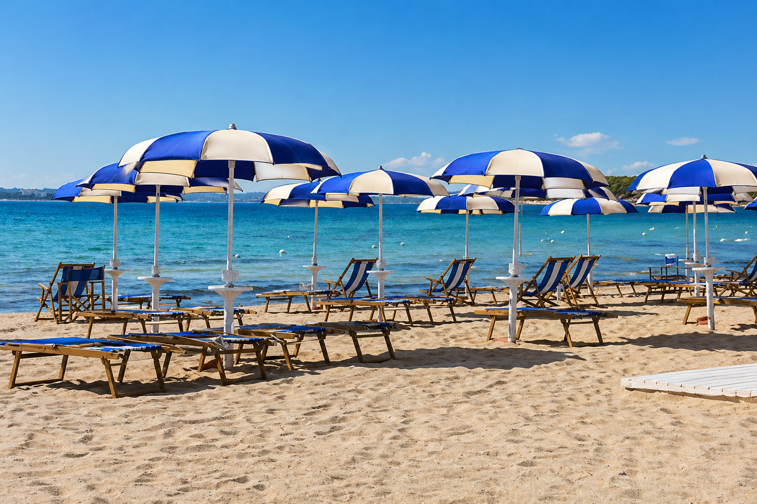 Spiaggia con ombrelloni e lettini blu e bianchi in riva a un mare blu calmo.