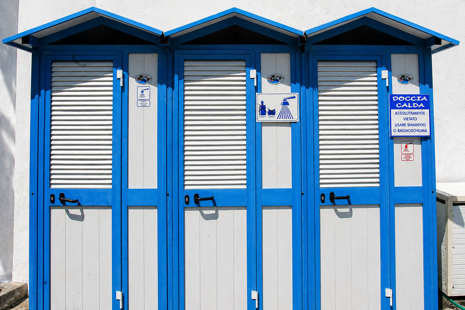 Una fila di cabine spogliatoio da spiaggia blu e bianche con porte chiuse a chiave e cartelli