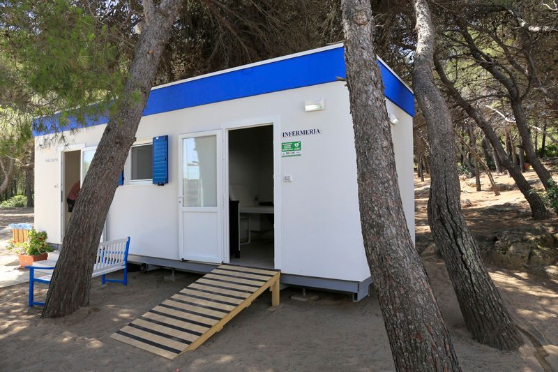 Piccola baita bianca con tetto blu immersa tra gli alberi, con porta aperta e rampa d'ingresso.