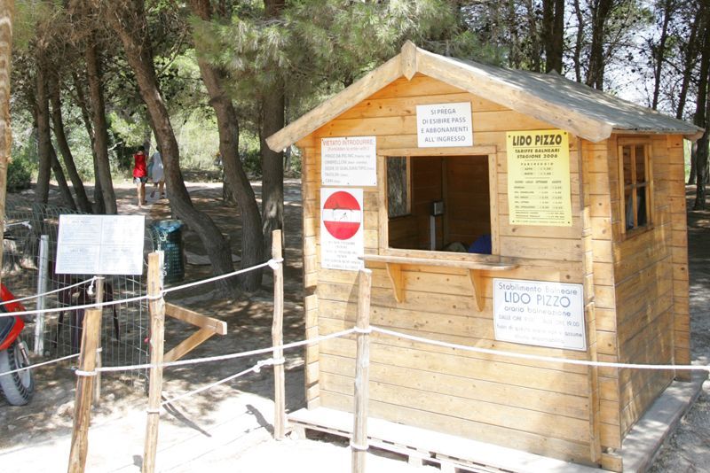 Piccola biglietteria in legno situata in una zona boschiva, con cartelli e una barriera di divieto d'accesso nelle vicinanze.