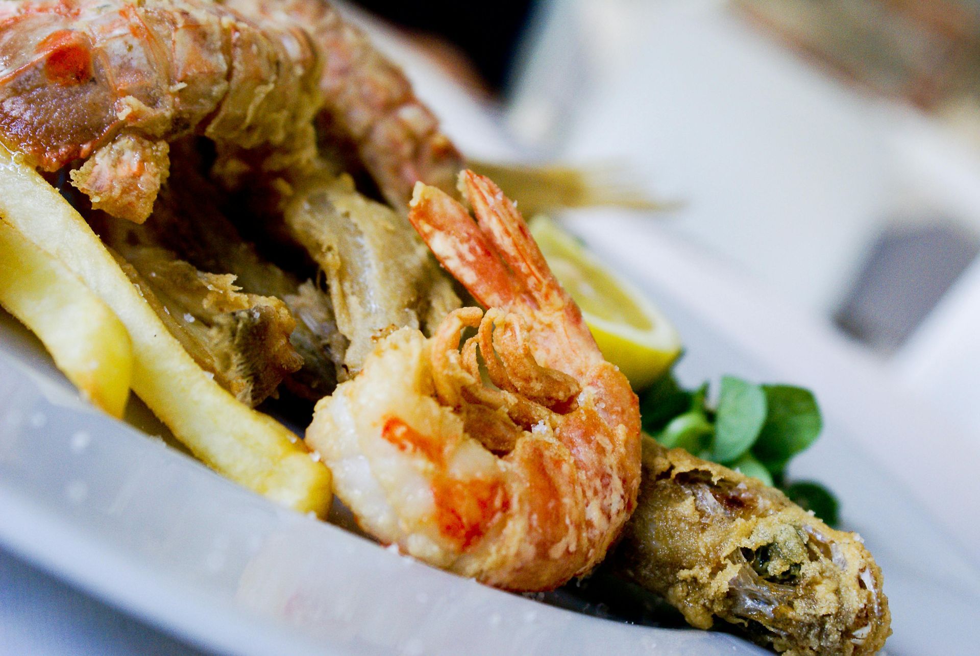 Primo piano di frutti di mare grigliati con gamberi e pesce su un piatto bianco, guarniti con limone e verdure.