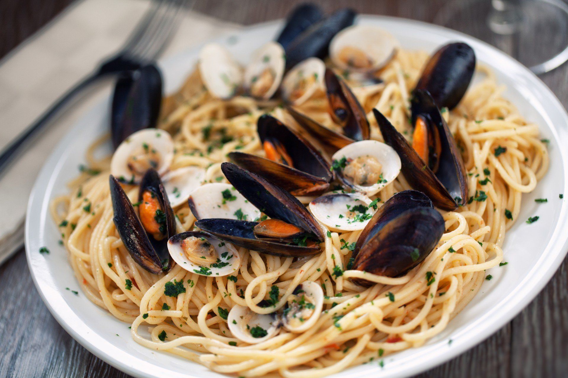 Piatto di spaghetti con cozze, vongole ed erbe aromatiche in un piatto bianco