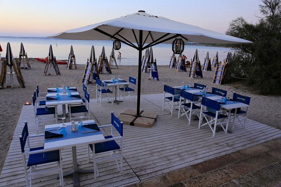 Tavolini e sedie blu in un caffè sulla spiaggia, sotto gli ombrelloni al tramonto.