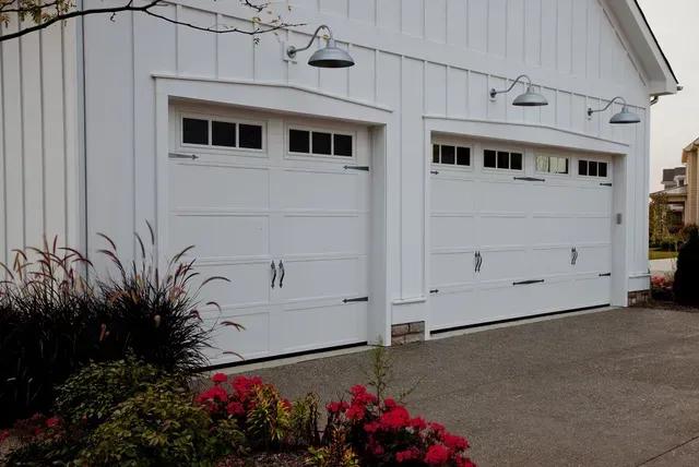 White garage doors on a house with flower beds and a paved driveway