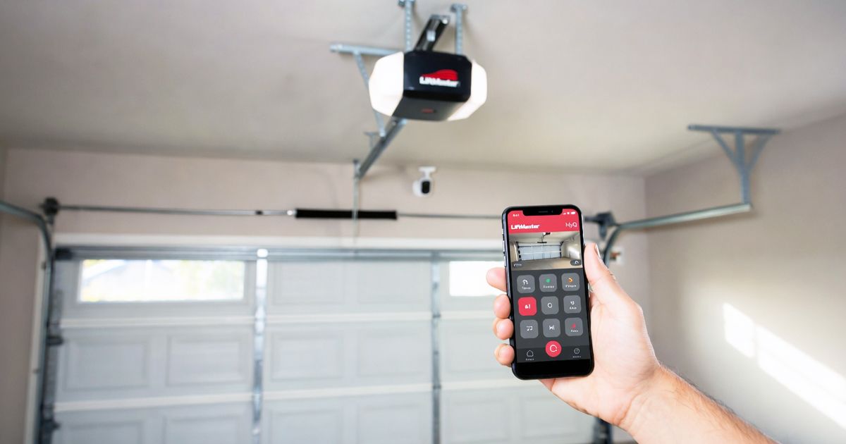 Hand holding a smartphone remote aimed at an open garage door opener in a garage