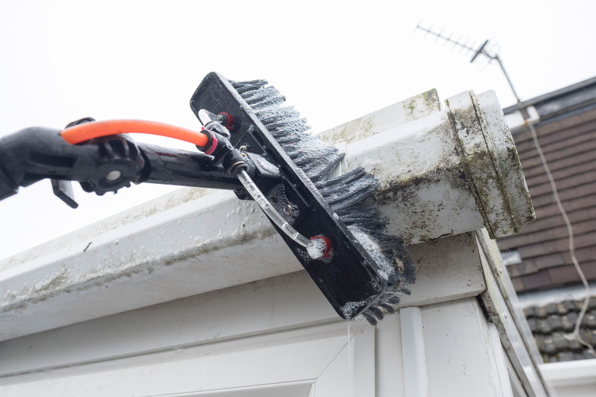 Person cleaning a house gutter with a long-handled brush