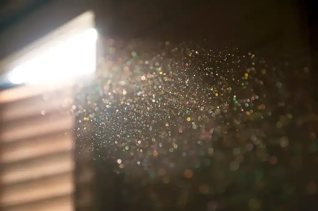 A ray of sun coming through the wooden shutters, illuminates dust on the inside of a dark room